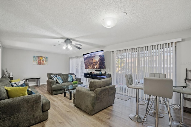 living room featuring ceiling fan, light hardwood / wood-style floors, and a textured ceiling