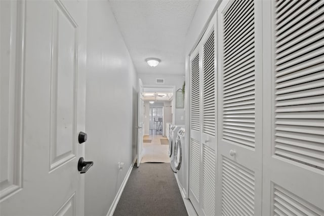 hallway with separate washer and dryer, a textured ceiling, and dark colored carpet