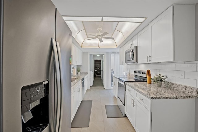 kitchen with ceiling fan, white cabinetry, stainless steel appliances, light stone countertops, and a raised ceiling