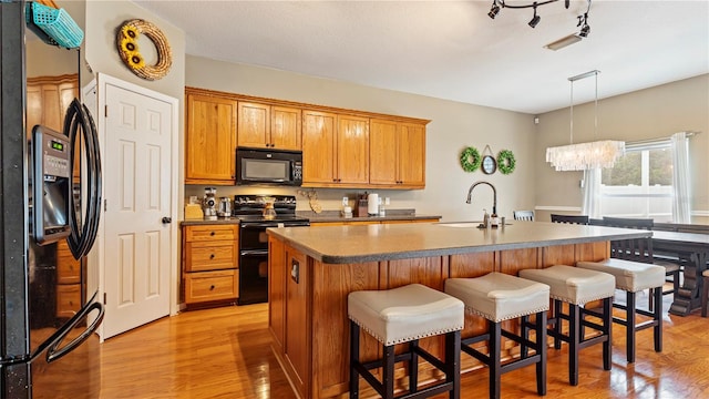 kitchen with sink, light hardwood / wood-style flooring, a kitchen island with sink, black appliances, and decorative light fixtures