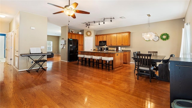 kitchen with dark hardwood / wood-style flooring, ceiling fan with notable chandelier, a breakfast bar area, and black appliances