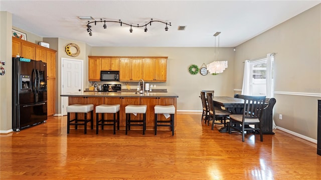 kitchen with an island with sink, dark wood-type flooring, sink, and black appliances