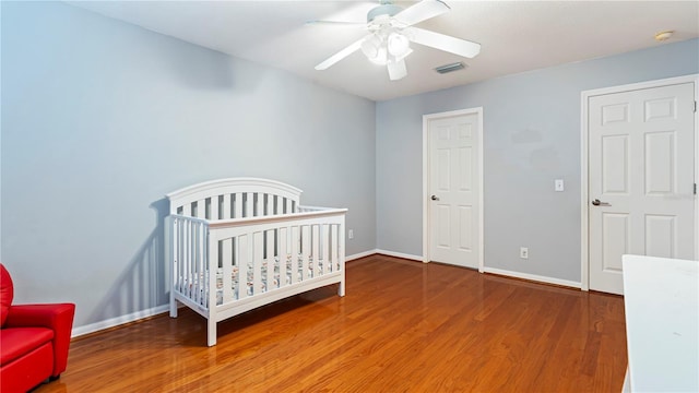 bedroom featuring hardwood / wood-style flooring, ceiling fan, and a crib