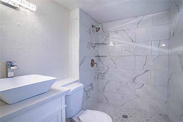 bathroom with a tile shower, vanity, and toilet