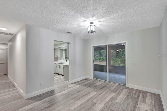 unfurnished room with light hardwood / wood-style floors, sink, and a textured ceiling