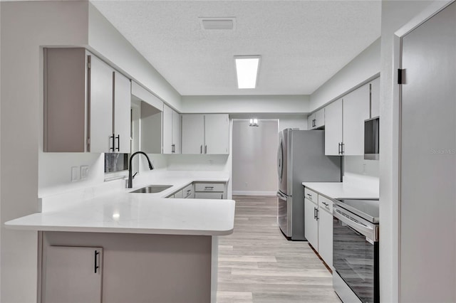 kitchen featuring stainless steel appliances, kitchen peninsula, sink, and a textured ceiling