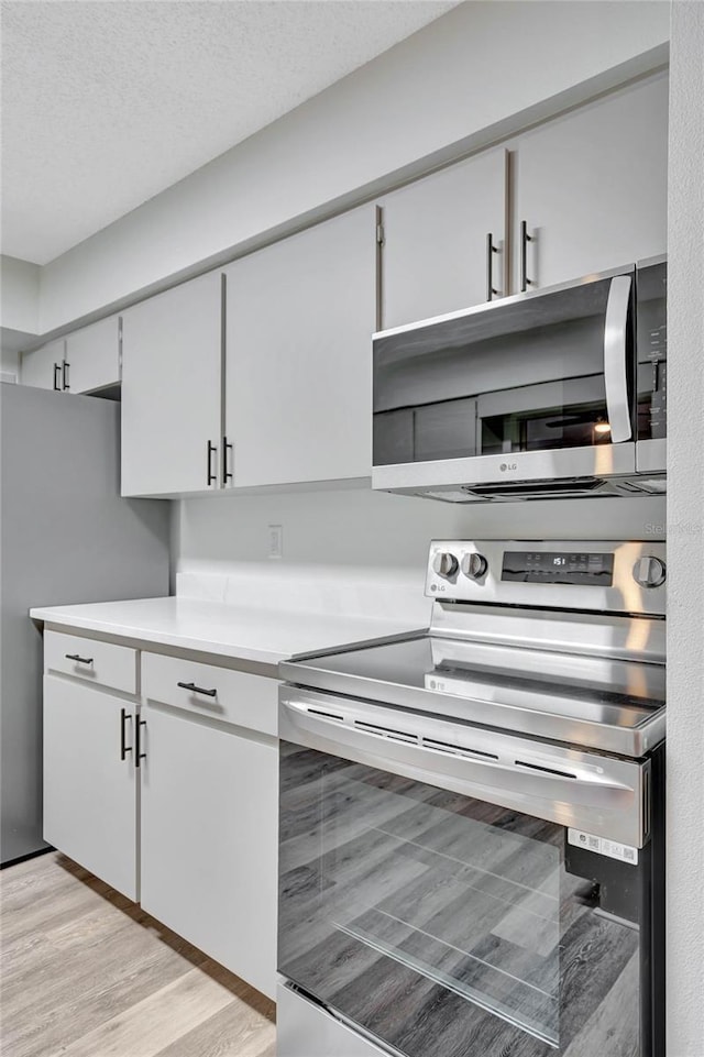 kitchen with appliances with stainless steel finishes, light hardwood / wood-style floors, and a textured ceiling