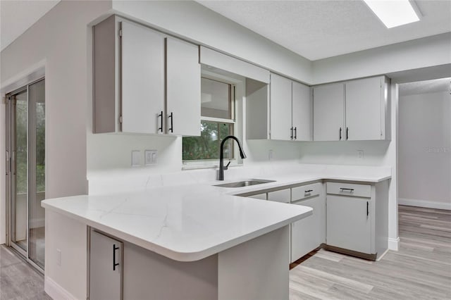 kitchen with kitchen peninsula, sink, light hardwood / wood-style flooring, and a textured ceiling