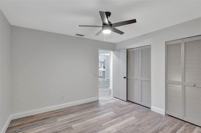 unfurnished bedroom featuring ceiling fan, light hardwood / wood-style flooring, and two closets