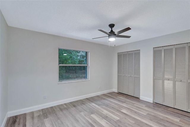 unfurnished bedroom with two closets, a textured ceiling, ceiling fan, and light wood-type flooring