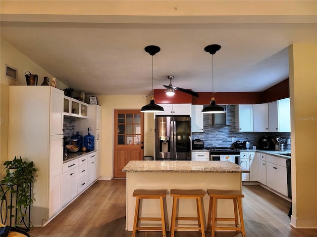 kitchen with a kitchen bar, a kitchen island, pendant lighting, stainless steel appliances, and white cabinets