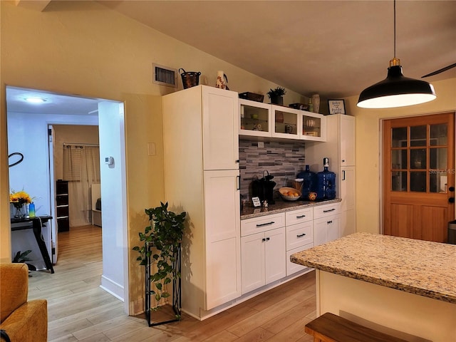 kitchen featuring pendant lighting, white cabinetry, lofted ceiling, light stone counters, and light hardwood / wood-style flooring