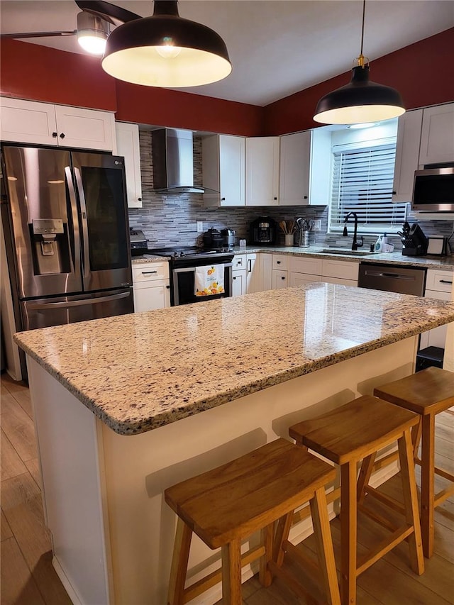 kitchen with white cabinetry, appliances with stainless steel finishes, a kitchen bar, and wall chimney exhaust hood