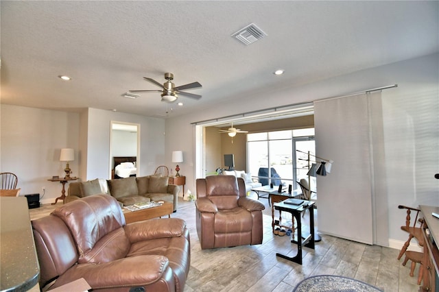 living room with ceiling fan, a textured ceiling, and light wood-type flooring