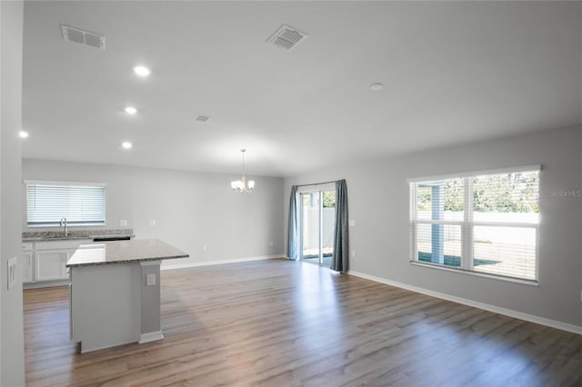 kitchen with a kitchen island, decorative light fixtures, sink, white cabinets, and light hardwood / wood-style flooring