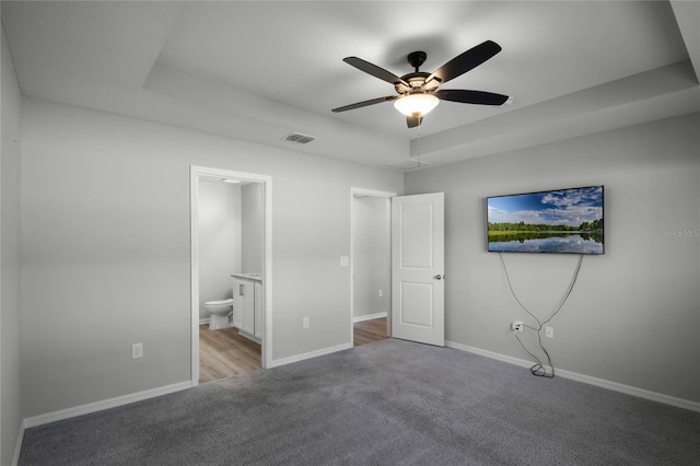 unfurnished bedroom with a raised ceiling, light colored carpet, ceiling fan, and ensuite bath