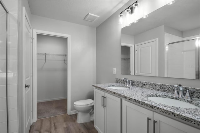 bathroom featuring a shower with shower door, hardwood / wood-style flooring, vanity, toilet, and a textured ceiling