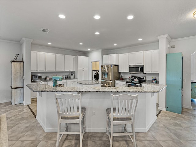 kitchen featuring a breakfast bar, a large island with sink, appliances with stainless steel finishes, washer / clothes dryer, and light stone countertops