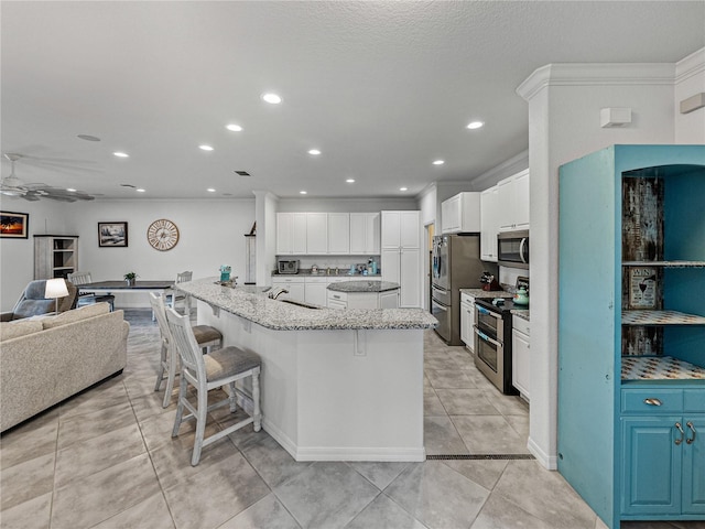 kitchen with a large island, a breakfast bar area, appliances with stainless steel finishes, light stone countertops, and white cabinets