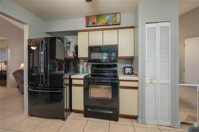 kitchen with light tile patterned flooring, tile counters, and black appliances