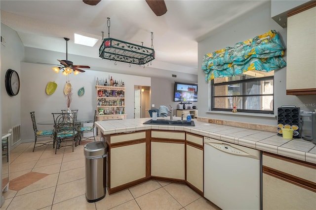 kitchen featuring sink, tile countertops, light tile patterned floors, dishwasher, and kitchen peninsula