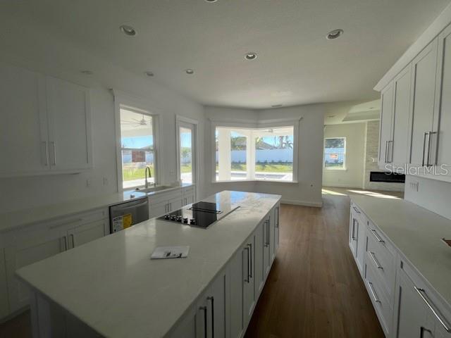 kitchen featuring black electric cooktop, dark wood-type flooring, light countertops, stainless steel dishwasher, and a center island