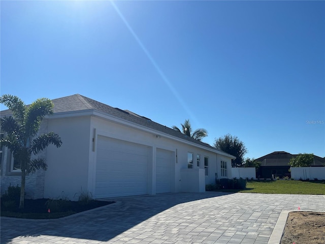 view of side of property with a lawn, an attached garage, fence, decorative driveway, and stucco siding