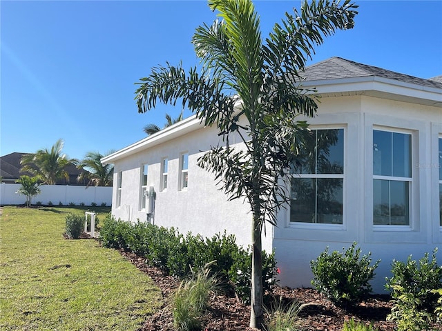 view of home's exterior featuring roof with shingles, fence, a lawn, and stucco siding