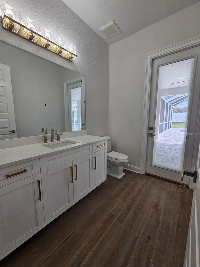 bathroom with toilet, a textured ceiling, vanity, wood finished floors, and baseboards