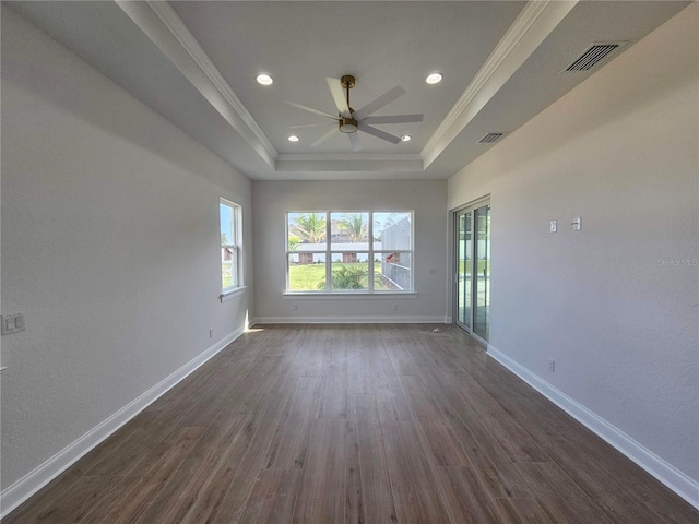 spare room featuring dark wood-style floors, a raised ceiling, visible vents, ornamental molding, and baseboards