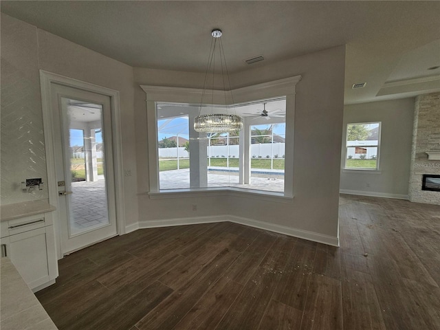 unfurnished dining area with dark wood-style floors, visible vents, a fireplace, and baseboards