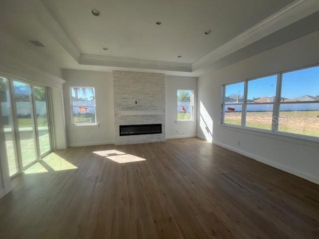 unfurnished living room with a large fireplace, wood finished floors, a raised ceiling, and baseboards