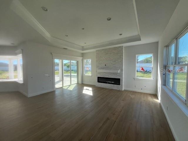 unfurnished living room featuring a raised ceiling, a healthy amount of sunlight, a stone fireplace, and wood finished floors