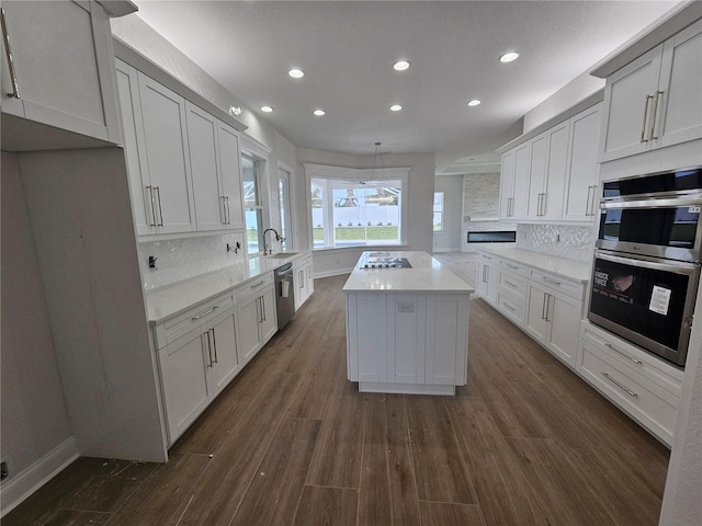 kitchen featuring stainless steel appliances, dark wood-style flooring, a sink, a kitchen island, and light countertops