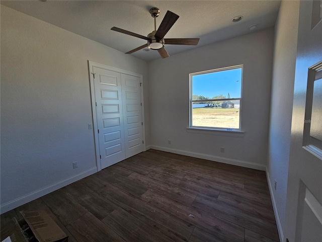 unfurnished bedroom featuring dark wood-style floors, ceiling fan, baseboards, and a closet