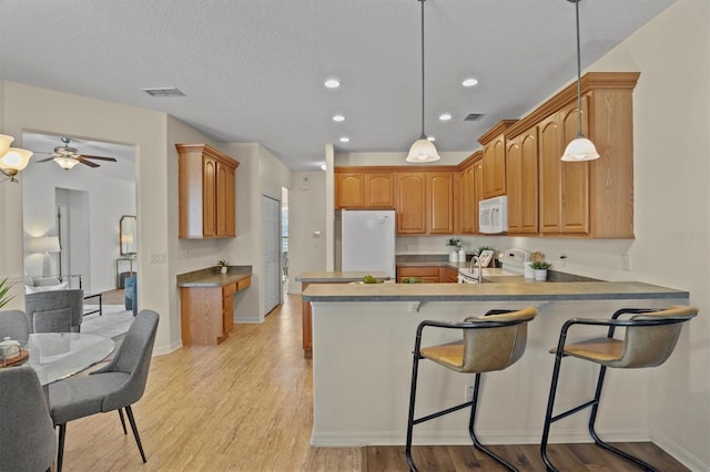 kitchen featuring pendant lighting, a breakfast bar area, white appliances, kitchen peninsula, and light wood-type flooring