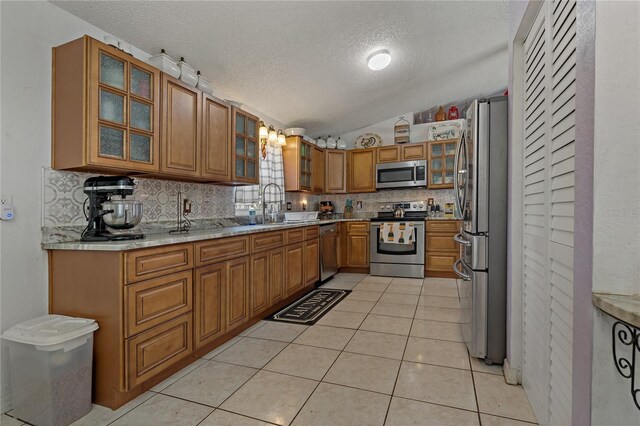 kitchen with sink, vaulted ceiling, light tile patterned floors, appliances with stainless steel finishes, and decorative backsplash