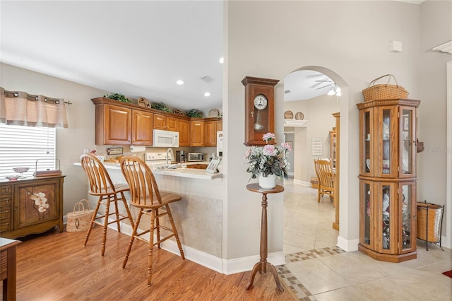 kitchen featuring white appliances, a kitchen bar, kitchen peninsula, and light hardwood / wood-style flooring