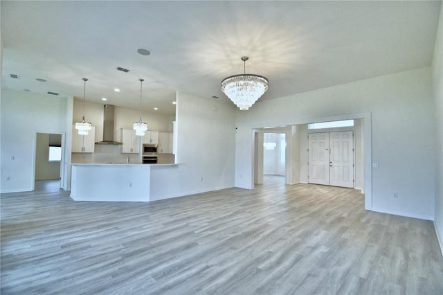 unfurnished living room featuring a notable chandelier and light wood-type flooring