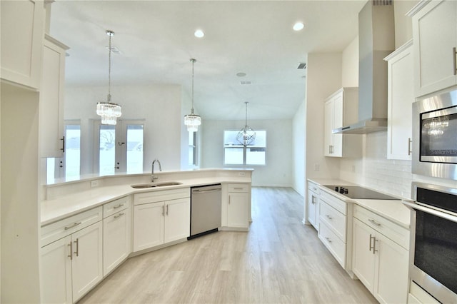 kitchen featuring wall chimney exhaust hood, appliances with stainless steel finishes, decorative light fixtures, and sink