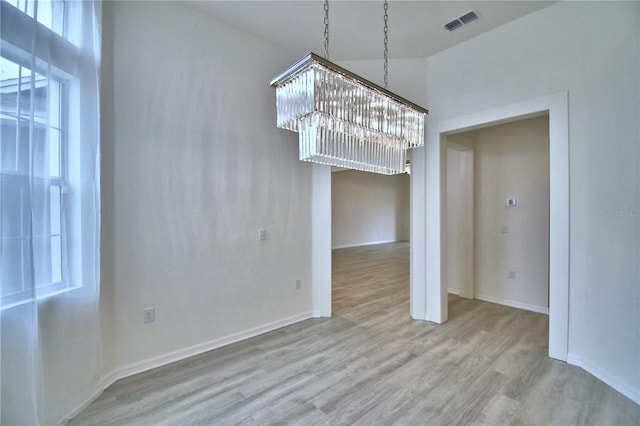 unfurnished dining area with a towering ceiling, an inviting chandelier, and light wood-type flooring