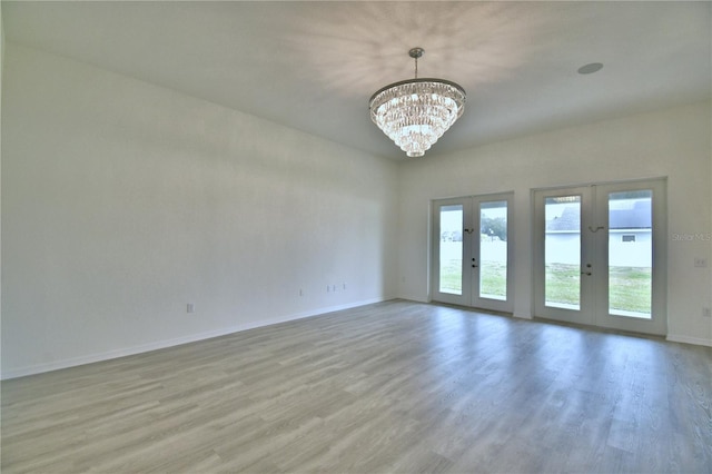 empty room with french doors, an inviting chandelier, and light wood-type flooring