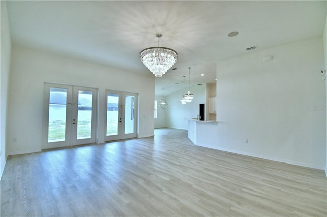 empty room with a notable chandelier, light wood-type flooring, and french doors