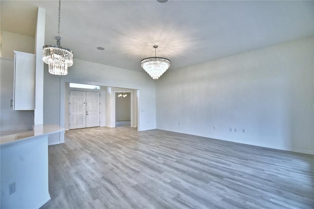 unfurnished living room featuring a notable chandelier and light wood-type flooring