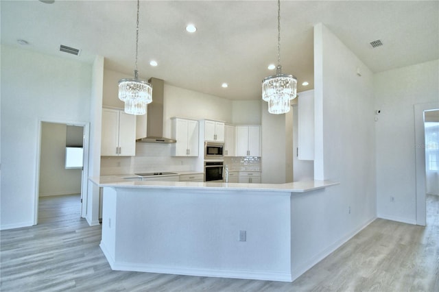 kitchen with appliances with stainless steel finishes, white cabinets, a chandelier, decorative backsplash, and wall chimney exhaust hood