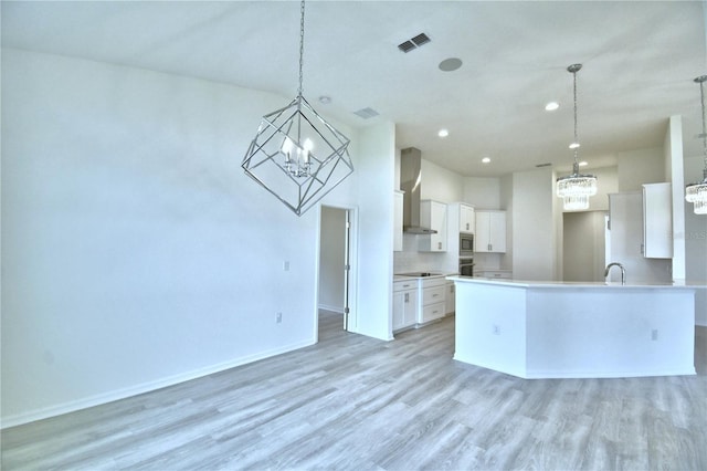 kitchen featuring white cabinetry, wall chimney range hood, light hardwood / wood-style flooring, and hanging light fixtures