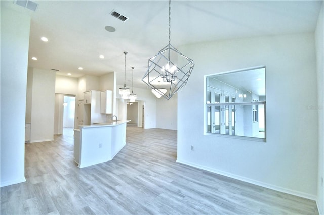 kitchen with pendant lighting, white cabinetry, light hardwood / wood-style flooring, and a notable chandelier