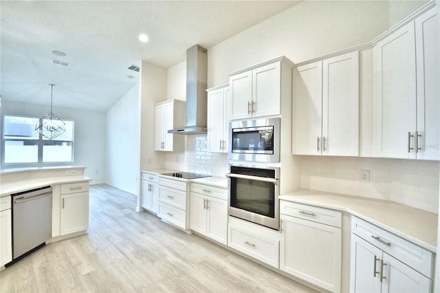 kitchen featuring wall chimney exhaust hood, white cabinetry, appliances with stainless steel finishes, pendant lighting, and backsplash