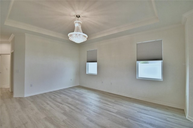 empty room with an inviting chandelier, light hardwood / wood-style floors, a raised ceiling, and a healthy amount of sunlight