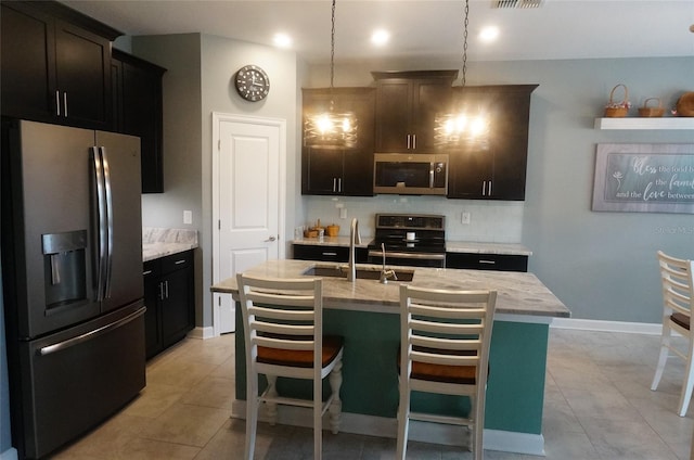 kitchen featuring a center island with sink, a sink, appliances with stainless steel finishes, light tile patterned flooring, and hanging light fixtures